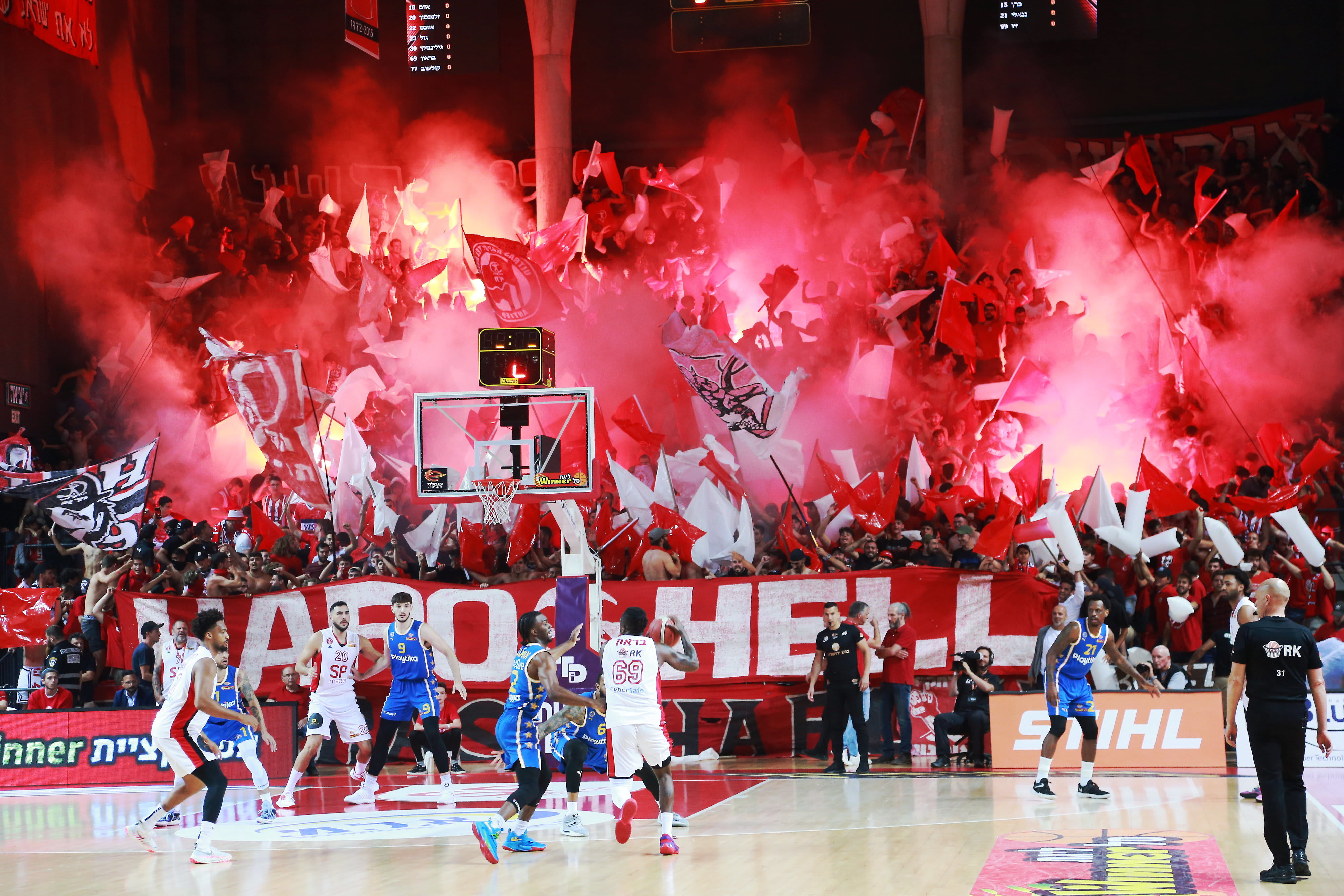 שחקני הפועל תל אביב מול שחקני מכבי תל אביב על רקע האבוקות ביציעים