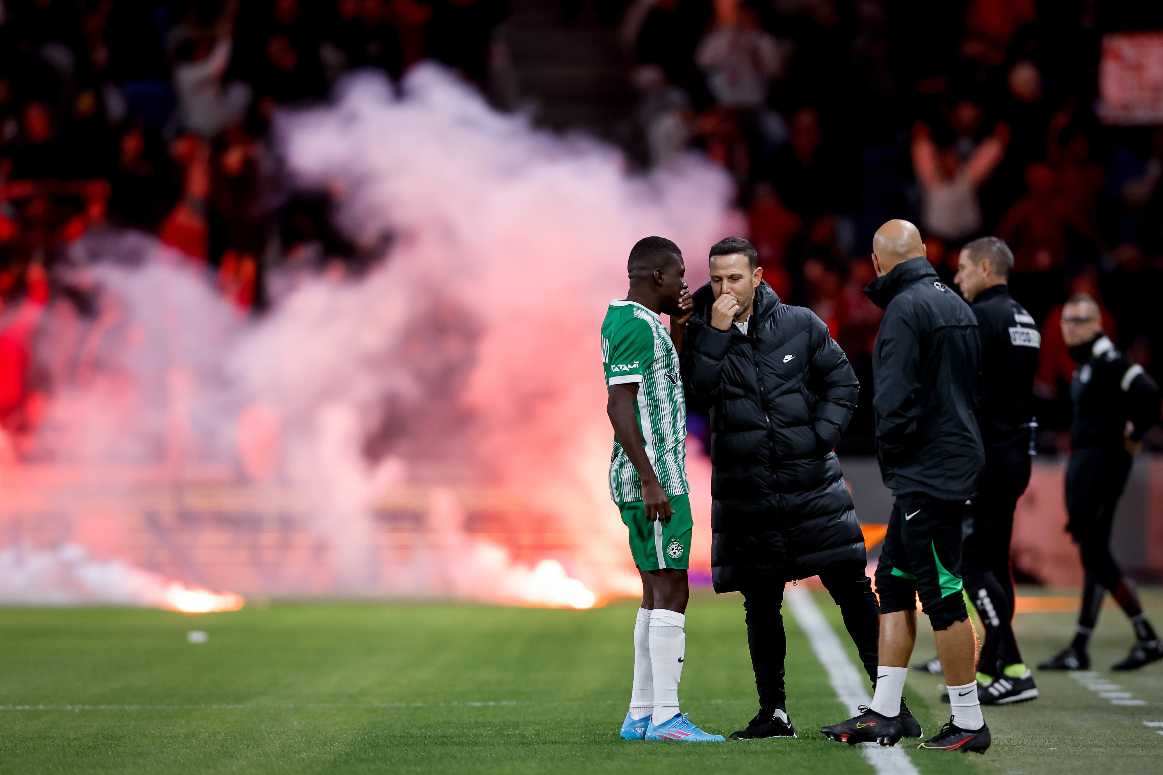 שחקן מכבי חיפה עלי מוחמד עם עוזר המאמן גיא צרפתי, על רקע רימוני עשן של אוהדי הפועל באר שבע