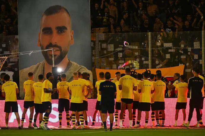 שחקני א.א.ק אתונה כשברקע תמונה של האוהד שנרצח, מיכאליס קאצוריס