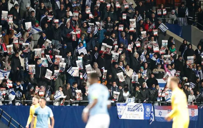 אוהדי נבחרת ישראל עם תמונות החטופים במשחק נגד רומניה