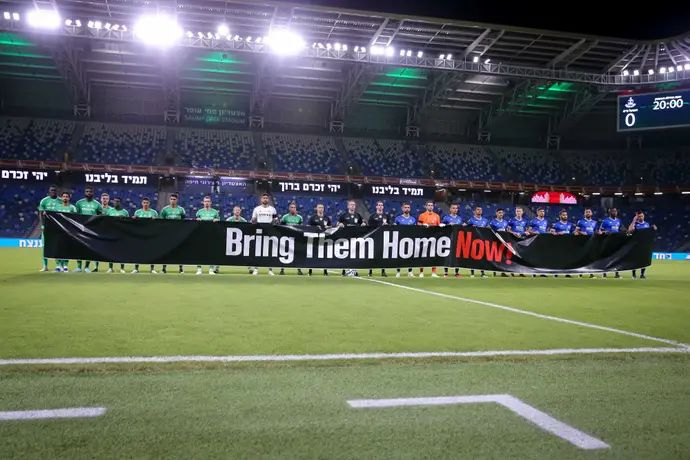 שחקני מכבי חיפה ושחקני הפועל פתח תקוה עם שלט הקורא להחזרת החטופים