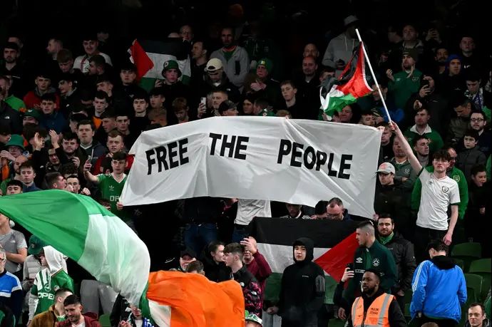 אוהדי נבחרת אירלנד מניפים כרזה ודגלי פלסטין