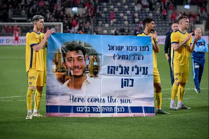 שחקני מכבי תל אביב עם שלט לזכרו של עילי אליהו כהן ז"ל, שנפל בקרב ברצועת עזה