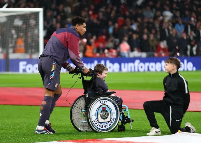 שחקן נבחרת אנגליה ג'וד בלינגהאם מעניק בגשם את המעיל שלו לילד על כיסא גלגלים