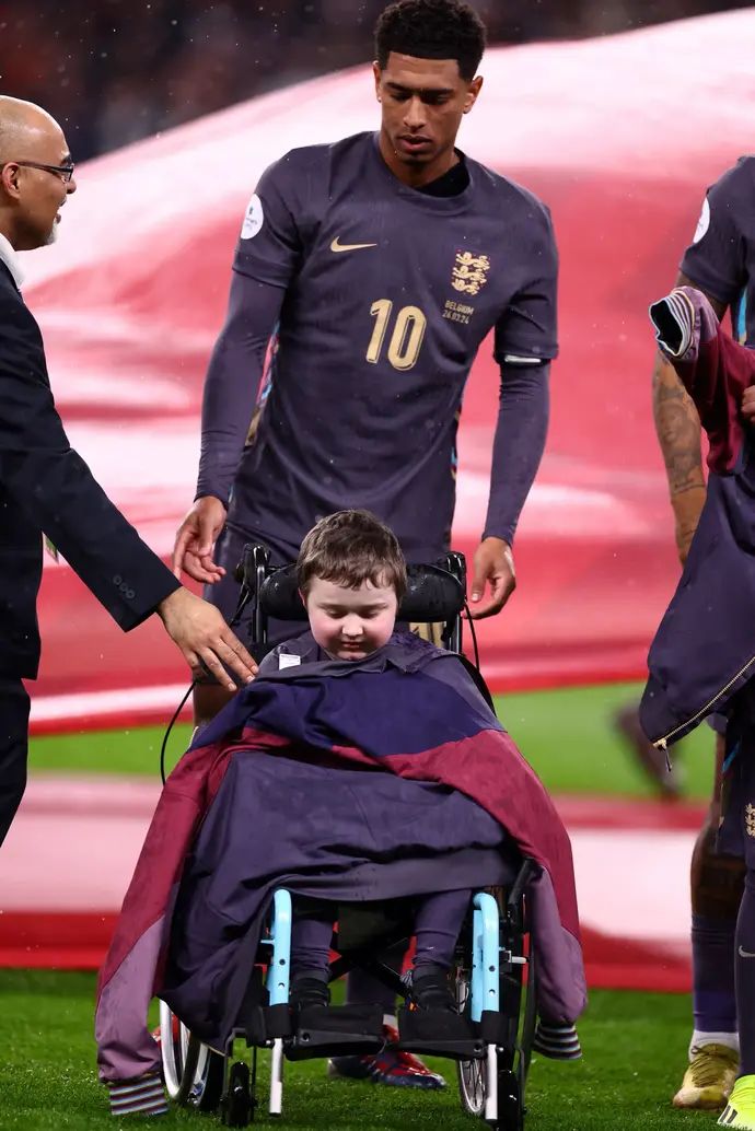 שחקן נבחרת אנגליה ג'וד בלינגהאם מעניק בגשם את המעיל שלו לילד על כיסא גלגלים