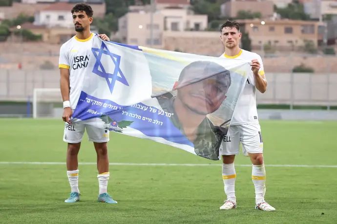 שחקני מכבי תל אביב, גבי קניקובסקי, רוי רביבו, עם דגל לזכרו של סמל דולב חיים מלכה ז"ל