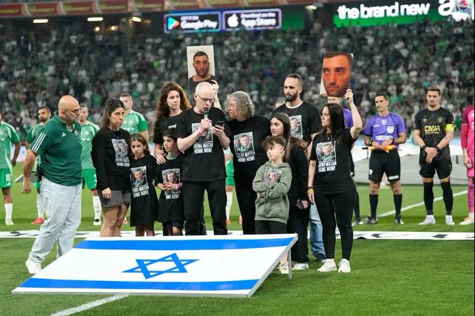 שורד השבי קית' סיגל במשחק של מכבי חיפה, קורא להשבת החטוף מתן אנגרסט, מימין אמו ענת אנגרסט