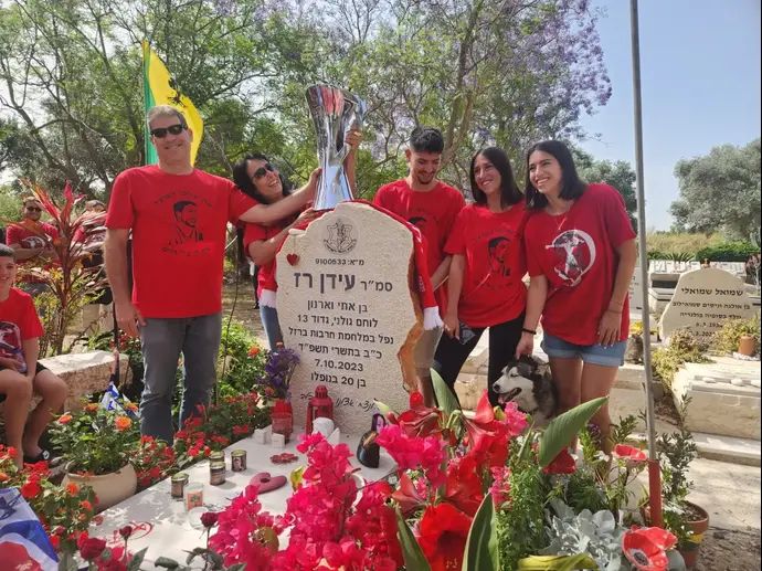 משפחתו של סמ"ר עידן רז, לצד קברו, עם גביע היורוקאפ בו זכתה הפועל תל אביב. יום הזיכרון 2025