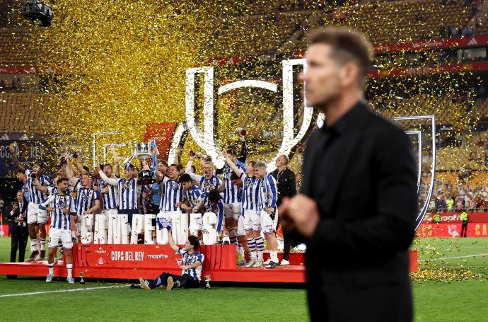 מאמן אתלטיקו מדריד דייגו סימאונה על רקע שחקני ריאל סוסיאדד מניפים את הגביע
